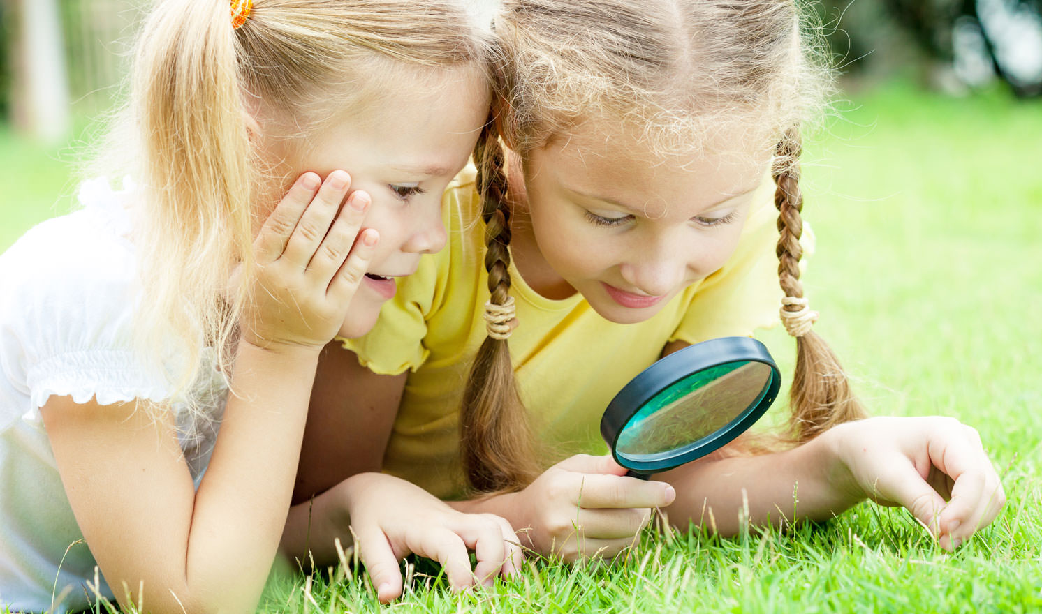 Zwei Kinder durchforschen das Gras mit einer Lupe